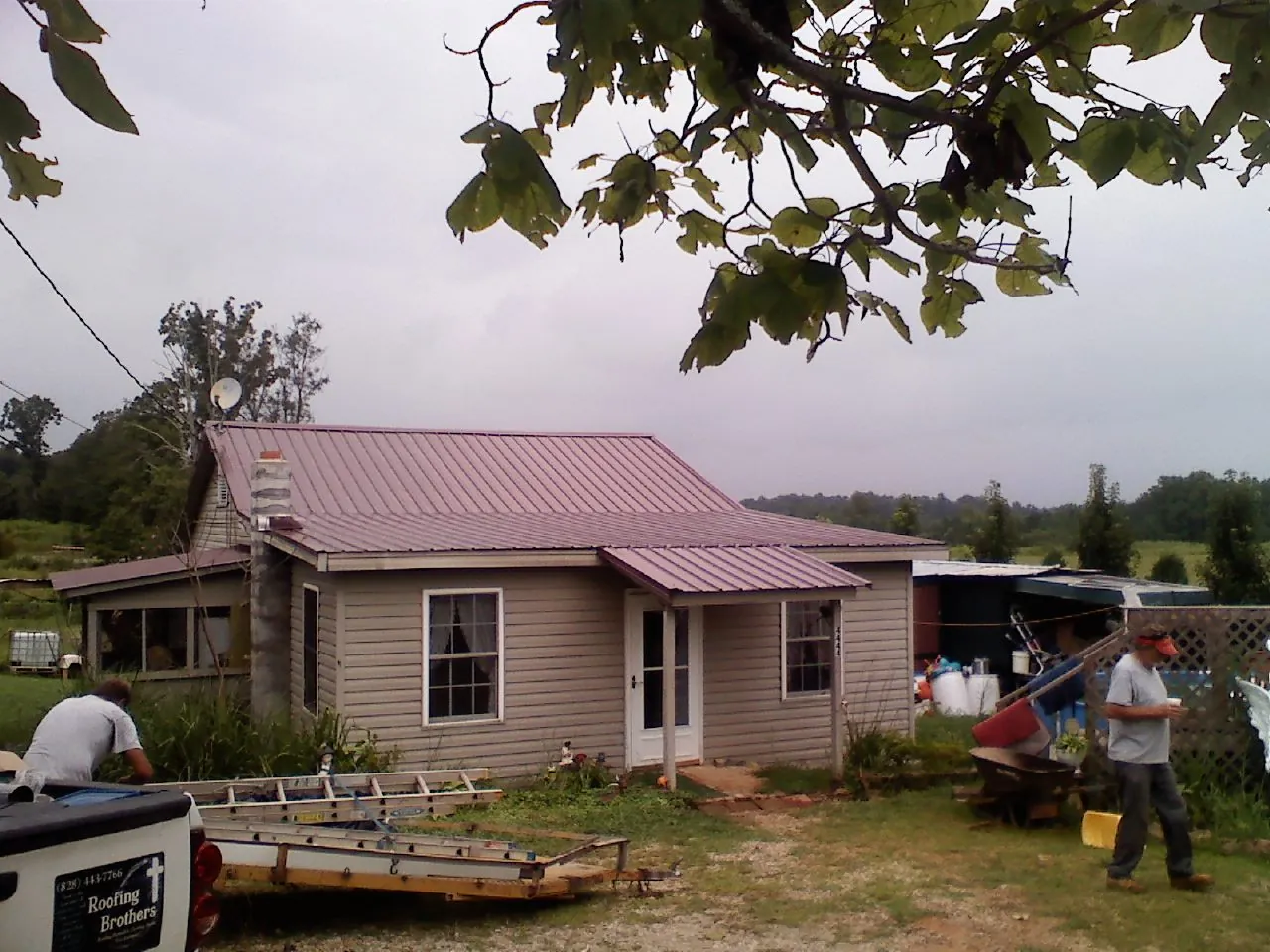 Crew finishing a mauve metal roof on a small farmhouse in Oneida