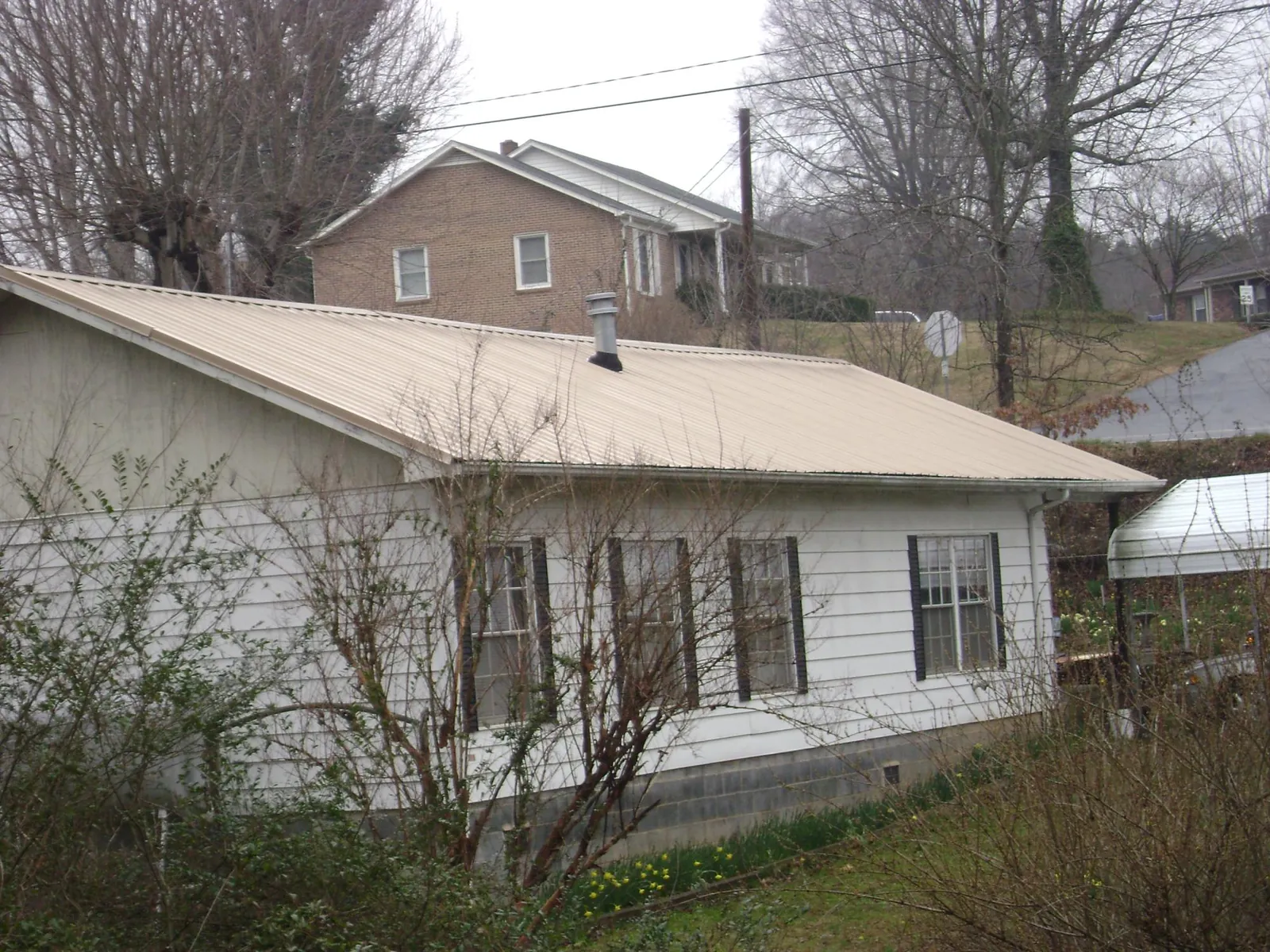 Tan metal roof on a white sided house set into a hillside — Commercial Roofing by Roofing Brothers in Oneida